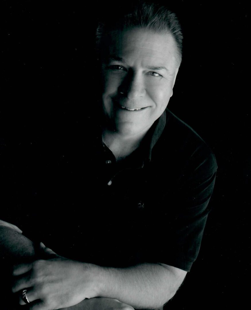 Black and white portrait of a man smiling with folded arms.