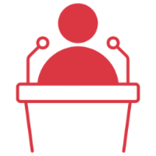 Silhouette of a person speaking at a podium with microphones.